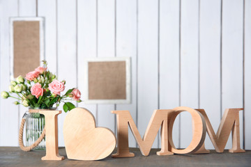 Fototapeta na wymiar I love mom inscription of wooden letters with heart and flowers on white wall background