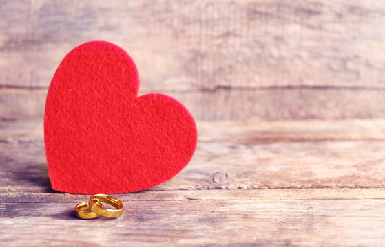 Red felt heart and wedding rings on wooden background closeup