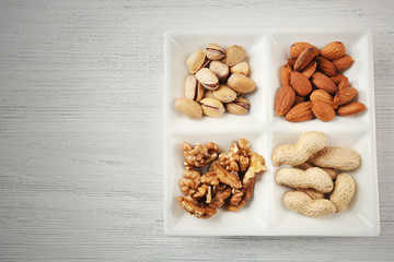 Walnut kernels, almonds, pistachios, peanuts in the ceramic rectangle plate on the wooden table
