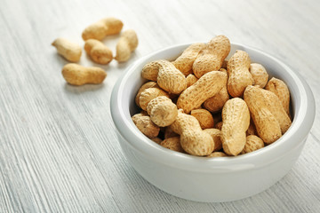 Peanuts in the bowl on white wooden background