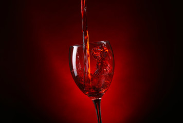 Wine pouring in glass on dark red background