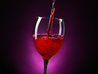 Wine pouring in glass on dark purple background