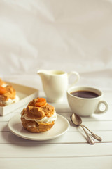 Homemade fresh cream puff with whipped cream and apricots, cup of coffee and milk jug. Toning.