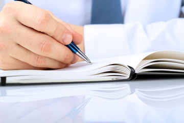 businessman writing in a notebook while sitting at a  his desk