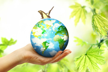 Globe on female human hand with butterfly in blur nature bokeh background with spfing leaves. Environment eco concept