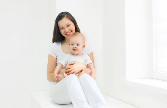 Happy smiling mother with baby at home in white room near window