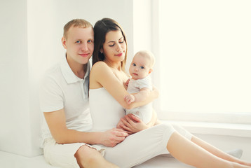 Happy family, mother and father with baby at home in white room