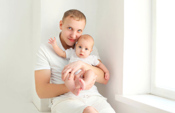 Happy young father and baby at home in white room near window