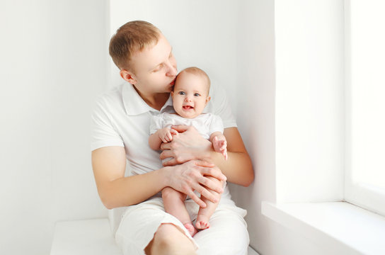 Happy young father with baby at home in white room near window