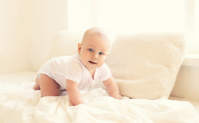 Cute baby crawls at home in white room near window