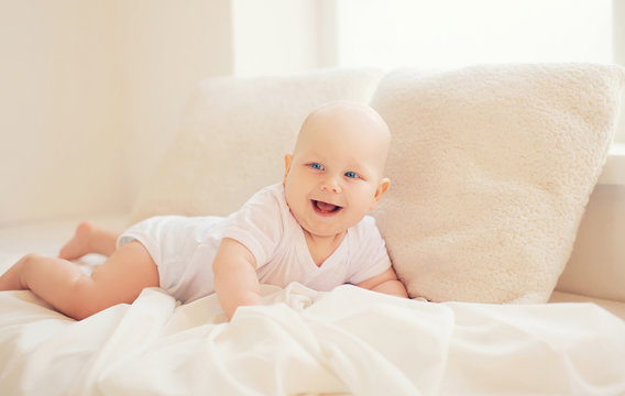 Happy smiling baby crawls at home in white room near window