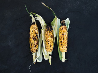 Grilled corn over black slate stone background, top view.