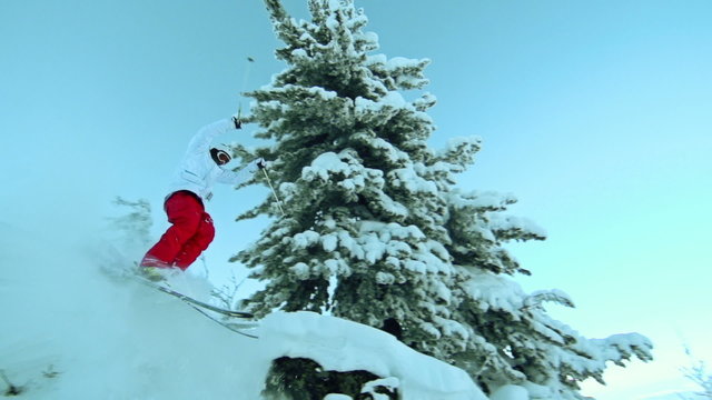 Low angle view of skier jumping from the hill and landing in cloud of snow dust