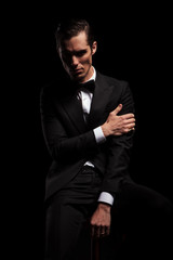 businessman pose seated in dark studio touching his arm