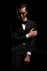 attractive man in black pose seated touching his arm