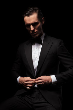 classy businessman in black suit posing seated in dark studio