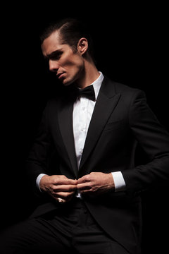 businessman in black suit with bowtie posing seated in dark
