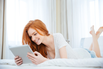 Smiling woman using tablet computer on the bed