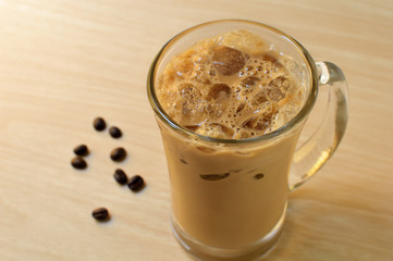 Cold coffee with ice in glass on a wooden background