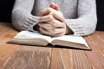 Woman hands praying with a bible in dark over wooden table