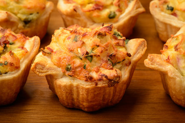 Tartlets baked with mashed potato, cheese, ham and parsley, on wooden background.
