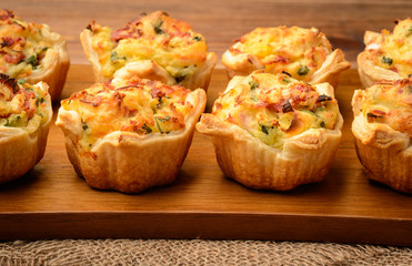 Tartlets baked with mashed potato, cheese, ham and parsley, on wooden background.