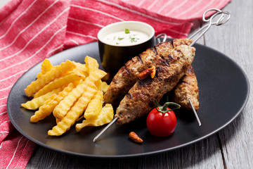 Barbecued kofta - kebeb with fries and vegetables on a plate.