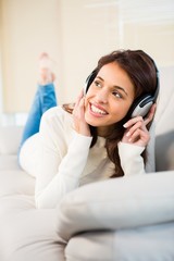 Pretty woman listening with headphones to music lying on couch
