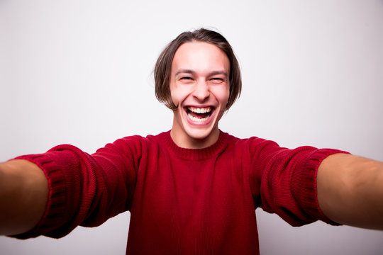 Selfie time! Handsome young man in red sweater camera and making selfie and smiling while standing against white background