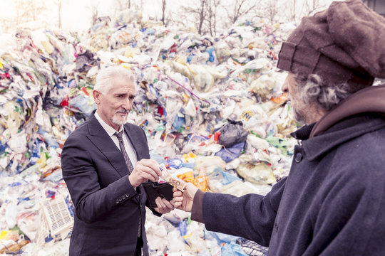businessman gives money to a homeless man in a dump