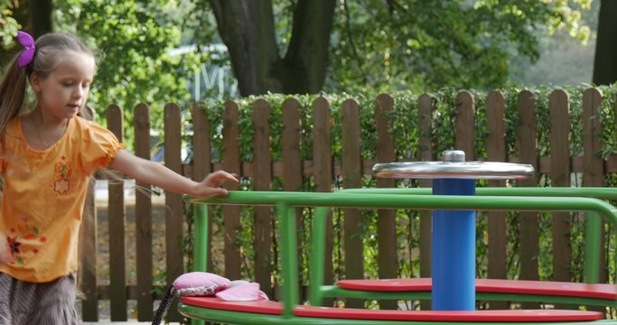 Girl is Rotating the Carousel Pink Toy Rabbit on Carousel Man Comes Little Girl With Long Fair Hairs in Orange T-Shirt is Playing s at the Playground