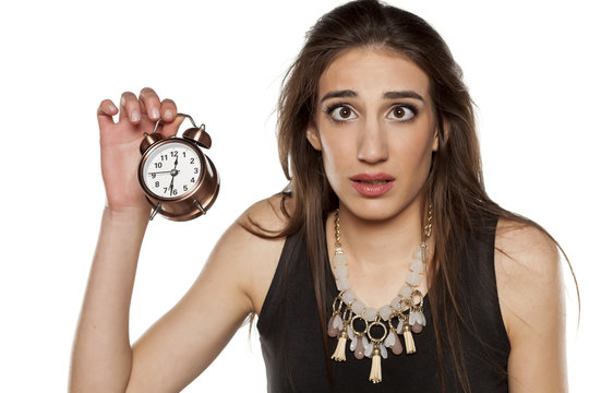 confused young woman holding alarm clock in her hand