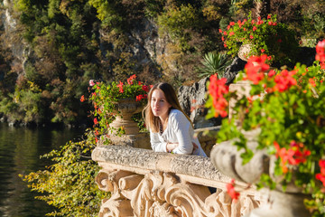 Young girl standing on the old terrace  balcony with flowers. Villa Balbianello in Lenno, Lake Como, Italy