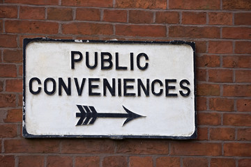 Public Convenience sign with pointing arrow on outside wall in a English village