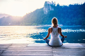 Foto op Plexiglas Yoga lotus. Jonge vrouw doet yoga aan het meer, zittend in lotus. © Microgen