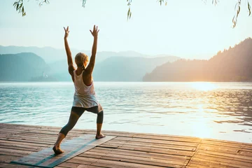  Yoga Sun Salutation. Young woman doing yoga by the lake at sunset, saluting to the sun.  © Microgen