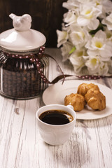 Coffee beans in vintage jar, cup of black coffee and pastry over wooden background. Toned image. Selective focus