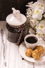 Coffee beans in vintage jar, cup of black coffee and pastry over wooden background. Toned image. Selective focus