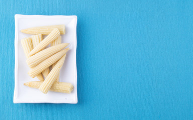 mini corn, canned lies on a rectangular white plate on a blue background