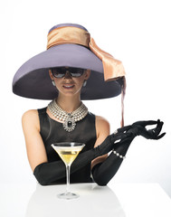 A woman in a big hat and sunglasses, like a movie star, drinking martinis