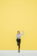 Happy proffesional woman celebrating business or job success against yellow wall. Trendy stylish modern businesswoman.