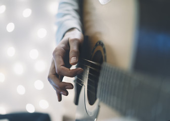 Сloseup of a man playing the guitar in a homelike atmosphere, sitting in a chair against a background of bokeh light horizontal