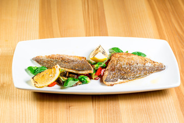 Tasty baked fish with grilled vegetables on  plate on wooden table close-up
