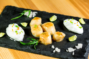 Studio close up of seared scallops, garnished with greens and sauce