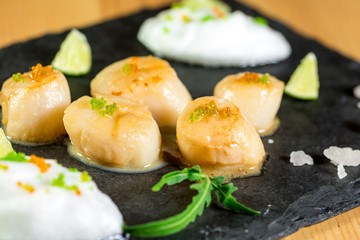 Studio close up of seared scallops, garnished with greens and sauce