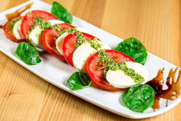 Caprese salad with mozzarella, tomato, basil and balsamic vinegar arranged on white plate