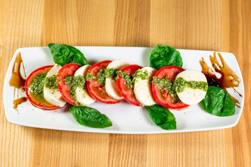 Caprese salad with mozzarella, tomato, basil and balsamic vinegar arranged on white plate