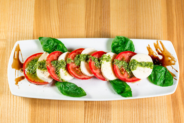 Caprese salad with mozzarella, tomato, basil and balsamic vinegar arranged on white plate