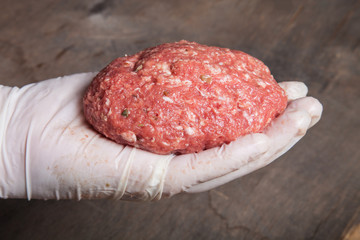 Hand in glove holding a raw cutlet. Shallow depth of field