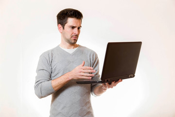 Junger Mann schaut mistrauisch auf einen Laptop im stehen 